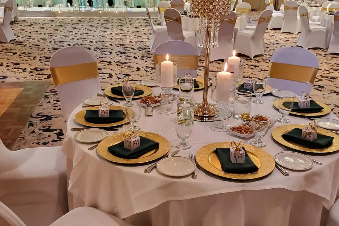 Close wedding place setting with gold charger plate, black napkin, gold favour box and a tall gold candelabra with pillar candles